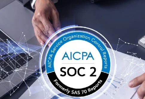 AICPA SOC 2 badge centered on a desk with hands, laptop, and documents, signaling trusted security controls.